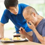 食事でせき込む高齢者と介助者